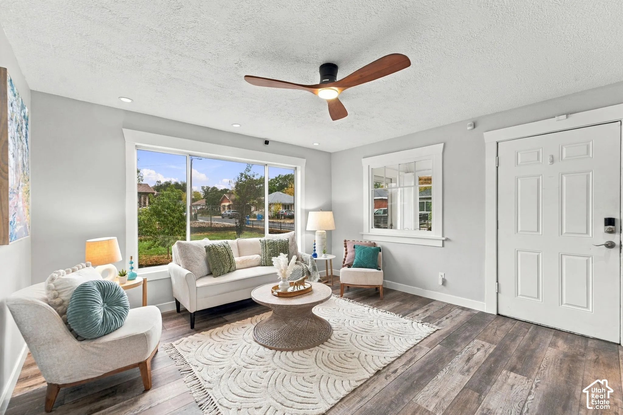 Wood-finish flooring, neutral wall tones, multi-pane window, flush-mounted ceiling fan with light fixture, and paneled entry door