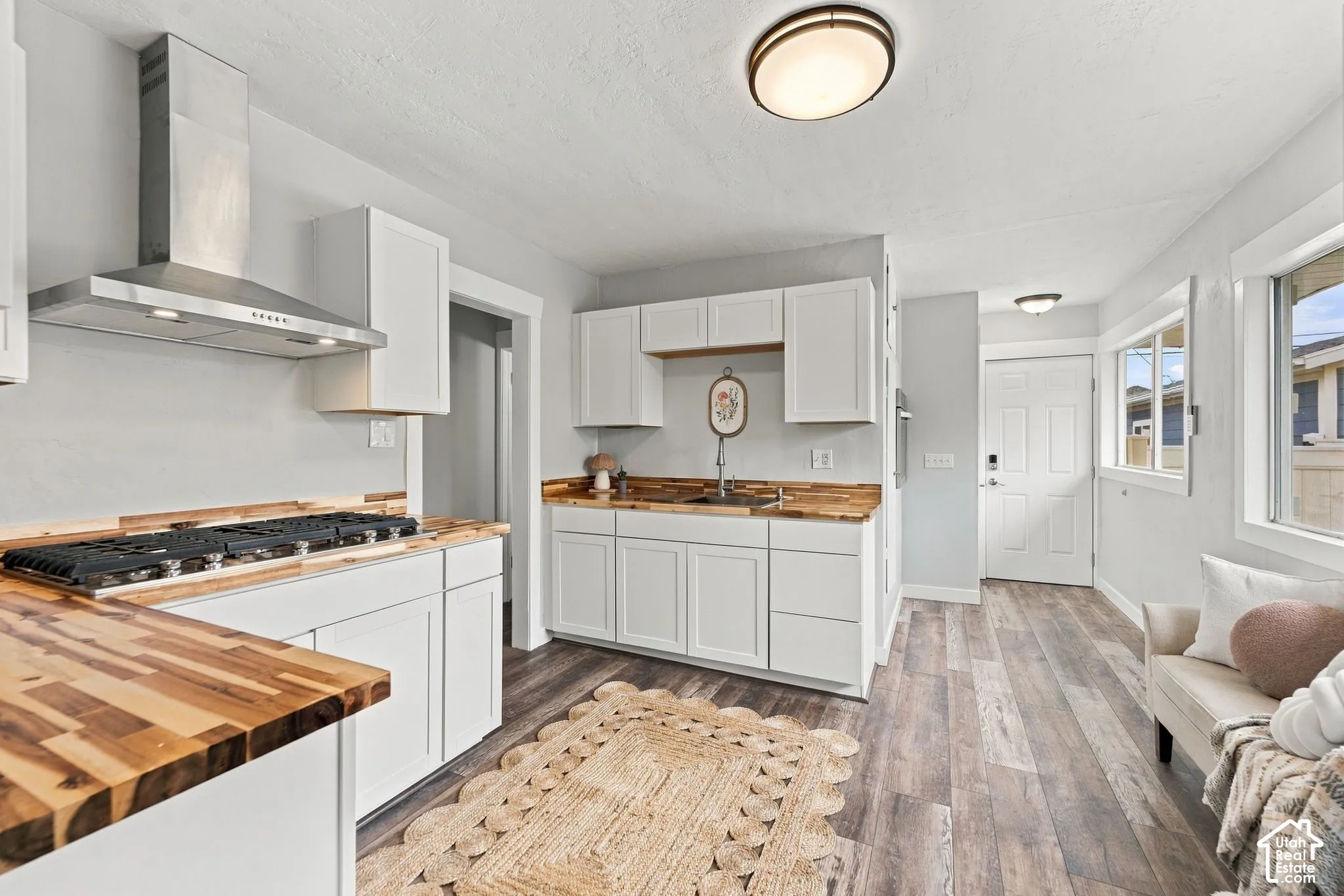 Kitchen featuring white shaker-style cabinetry, wood-finish countertops, a stainless steel gas cooktop, and a stainless steel wall-mounted range hood, complemented by wood-finish flooring