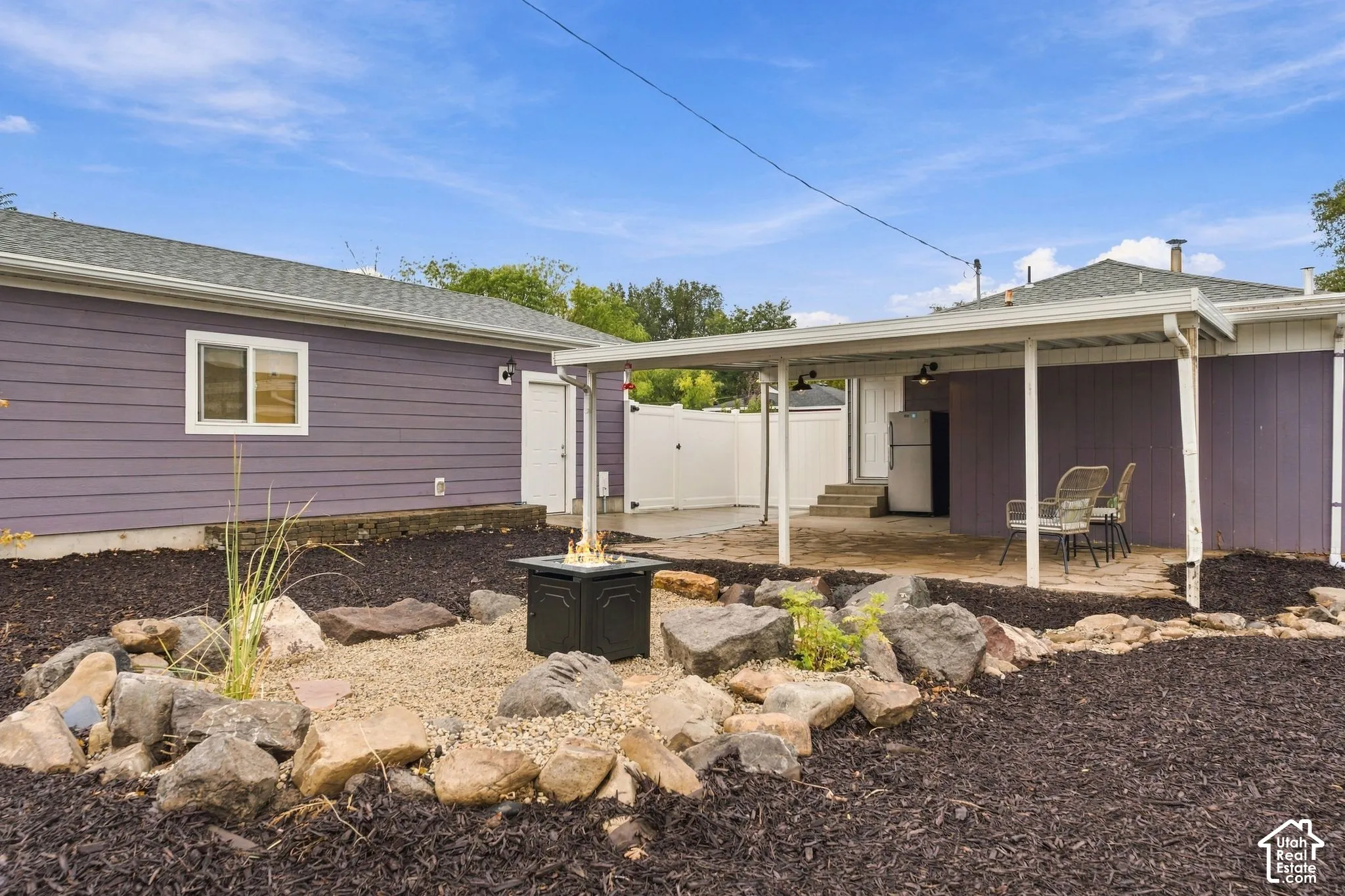 Backyard area featuring a covered stone patio, gravel landscaping with decorative rock borders, and a white privacy fence