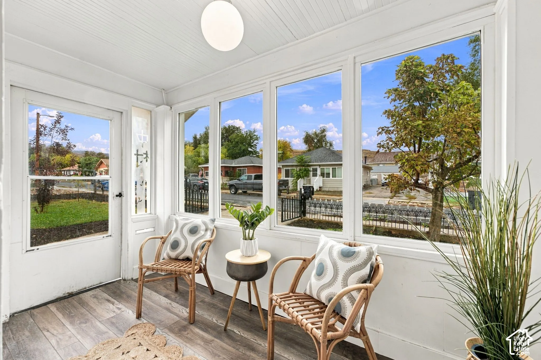 Enclosed sunroom featuring large-pane windows, wood-finish flooring, and a flush-mount globe light fixture