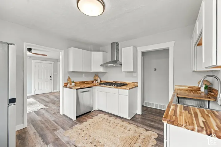 Kitchen featuring white shaker-style cabinetry, wood-finish countertops, stainless steel appliances, a stainless steel range hood, and wood-finish flooring