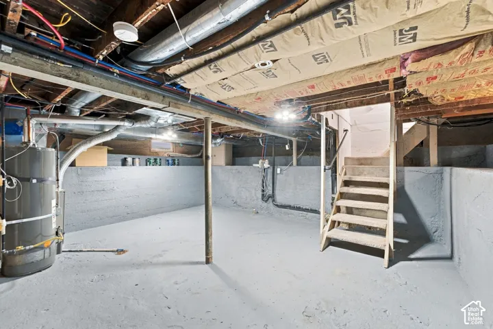 Unfinished basement featuring concrete flooring, painted foundation walls, exposed ceiling joists with insulation, and a water heater