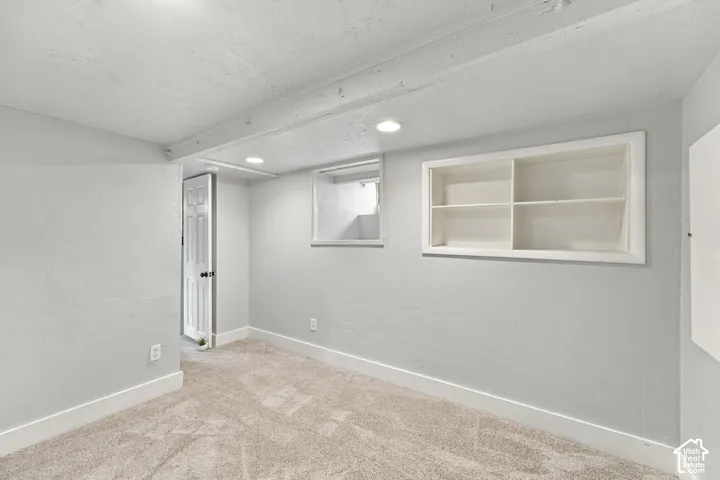 Neutral-toned interior space featuring wall-to-wall carpeting, recessed ceiling lighting, a built-in recessed wall shelf, and a single-pane window