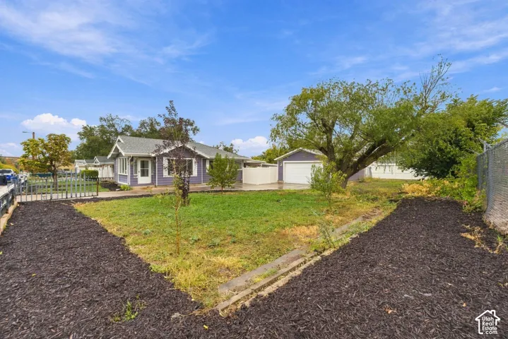 Single-story residence featuring a detached garage, concrete driveway, front lawn, and established trees