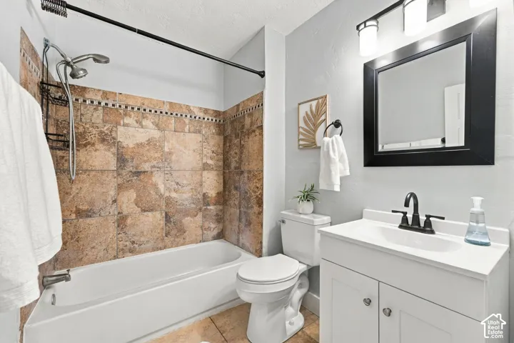 Bathroom featuring a tub-shower combination with floor-to-ceiling decorative tile surround, white vanity cabinet with a stone-finish countertop, matte black dual-handle faucet, and black-framed wall mirror
