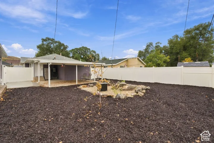 Private backyard featuring a covered patio, white vinyl fencing, mulched ground cover, and a rock-lined landscaping feature