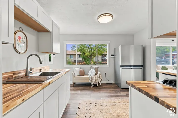 Kitchen featuring white shaker-style cabinetry, wood-surface countertops, stainless steel refrigerator, and wood-finish flooring