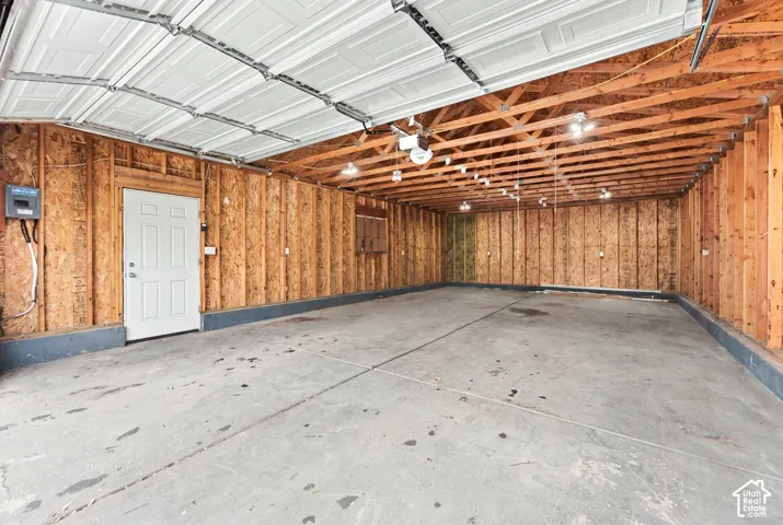 Multi-car garage featuring exposed wood-stud walls, a concrete floor, an overhead sectional door, and an integrated electrical service panel