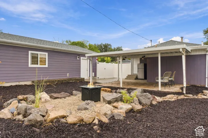 Backyard area featuring a covered stone patio, gravel landscaping with decorative rock borders, and a white privacy fence