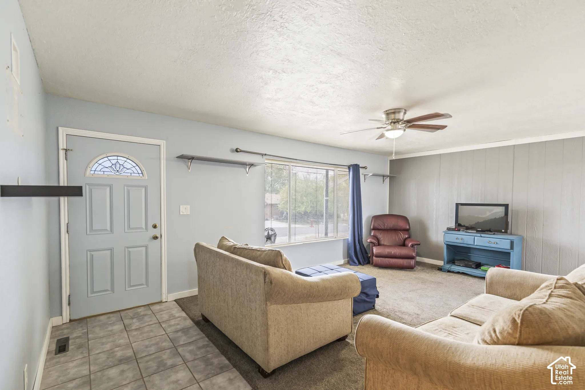 Entryway with tile flooring, wall-to-wall carpeting, ceiling-mounted fan, natural light from a large window, and paneled accent wall