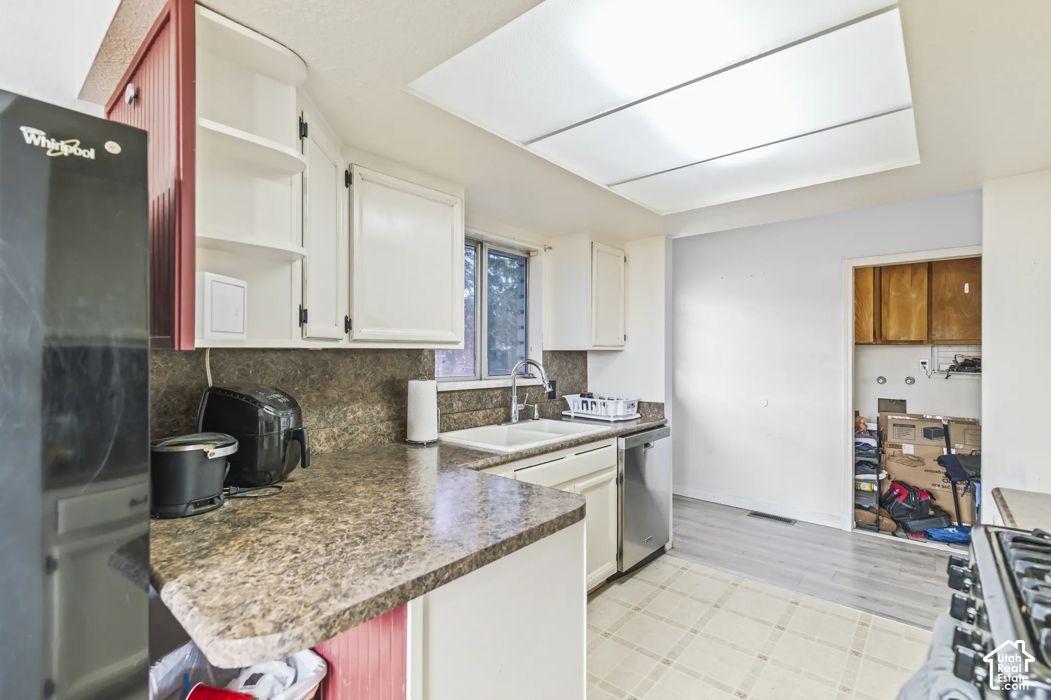 Kitchen featuring laminate countertops, dual-basin sink with gooseneck faucet, stainless steel dishwasher, and painted cabinetry