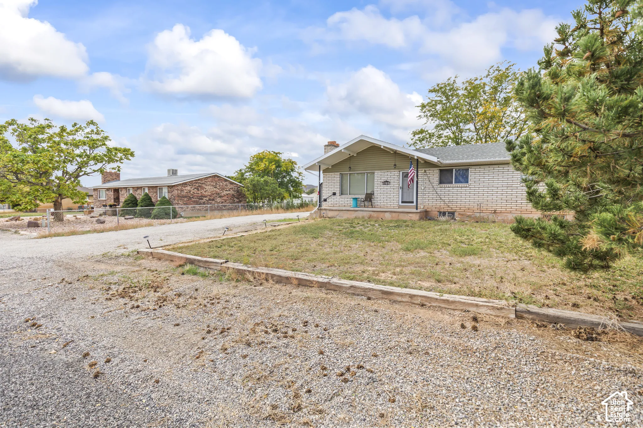 Single-story residence featuring a brick veneer exterior, covered front porch, timber retaining wall, and gravel driveway