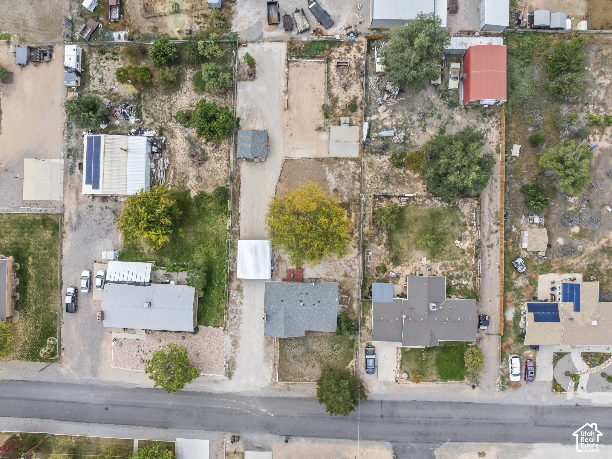 Aerial view of property featuring a gravel driveway, detached metal-roofed storage structure, fenced perimeter, and mature trees