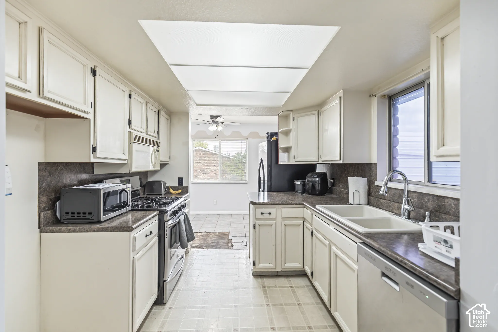 Kitchen featuring white cabinetry, dark-toned laminate countertops, a dual-basin sink with a gooseneck faucet, a built-in gas range, and recessed ceiling panel lighting