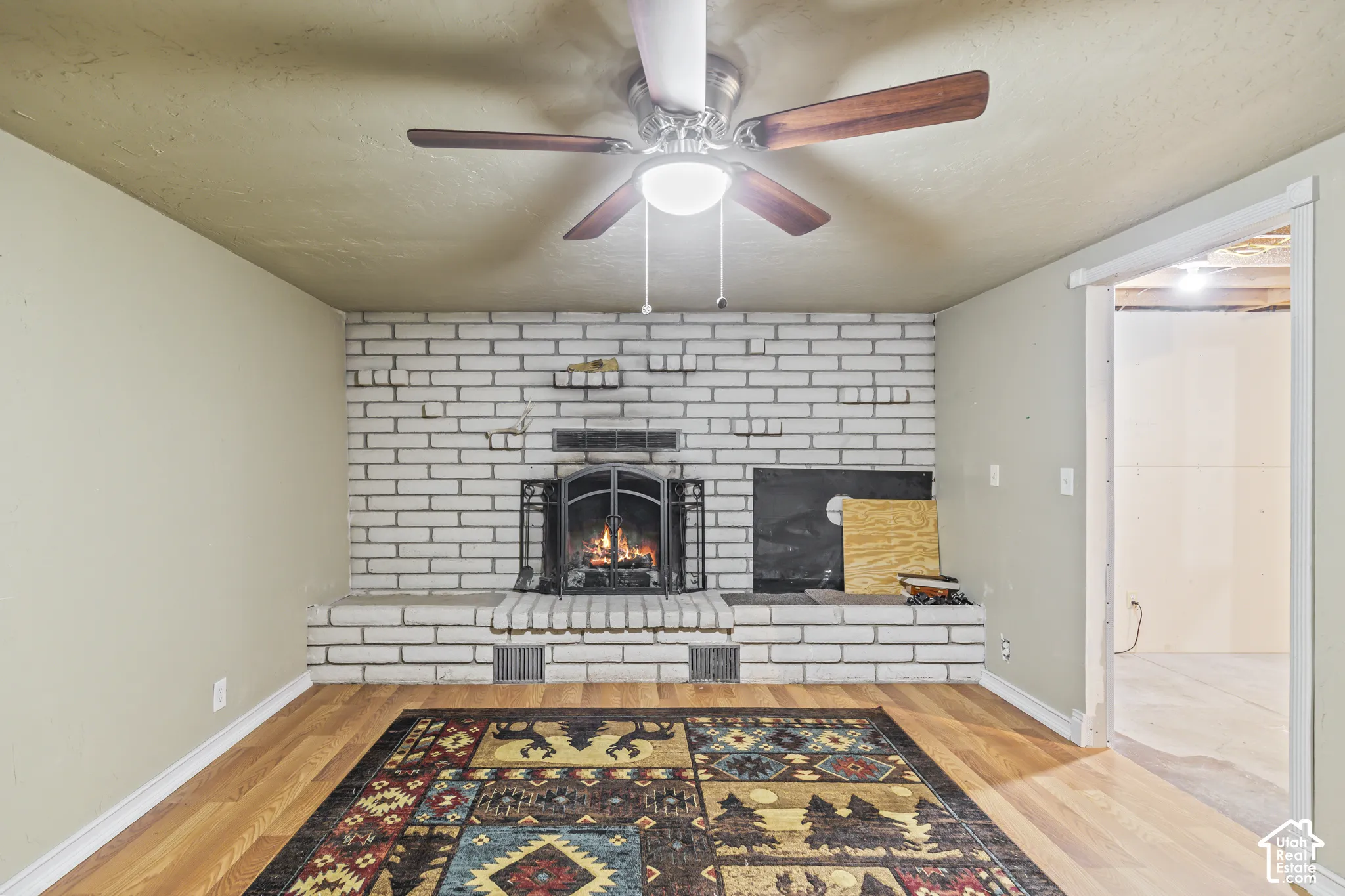 Painted brick fireplace with integrated hearth and decorative metal screen, complemented by a ceiling fan with integrated lighting and wood-finish flooring