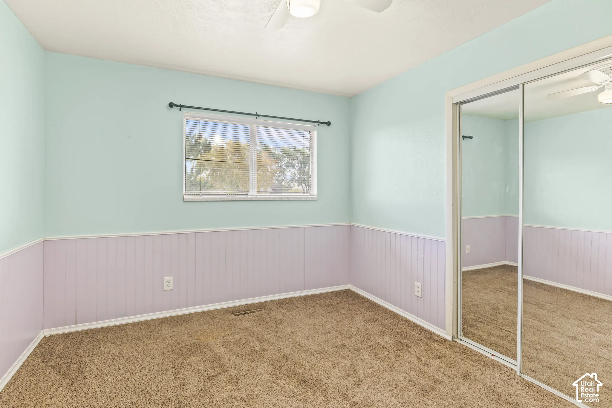 Room featuring wall-to-wall carpeting, beadboard wainscoting, a single-pane window, and floor-to-ceiling mirrored sliding closet doors