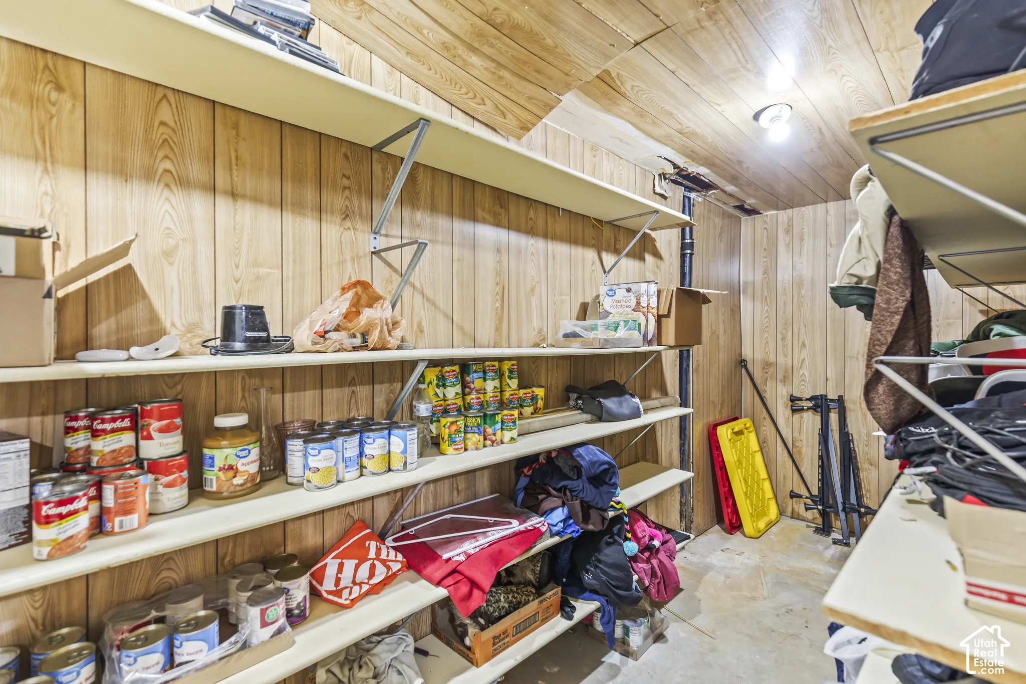 Storage space featuring wood-panel wall treatment, ceiling paneling, and multiple levels of built-in shelving with metal support brackets