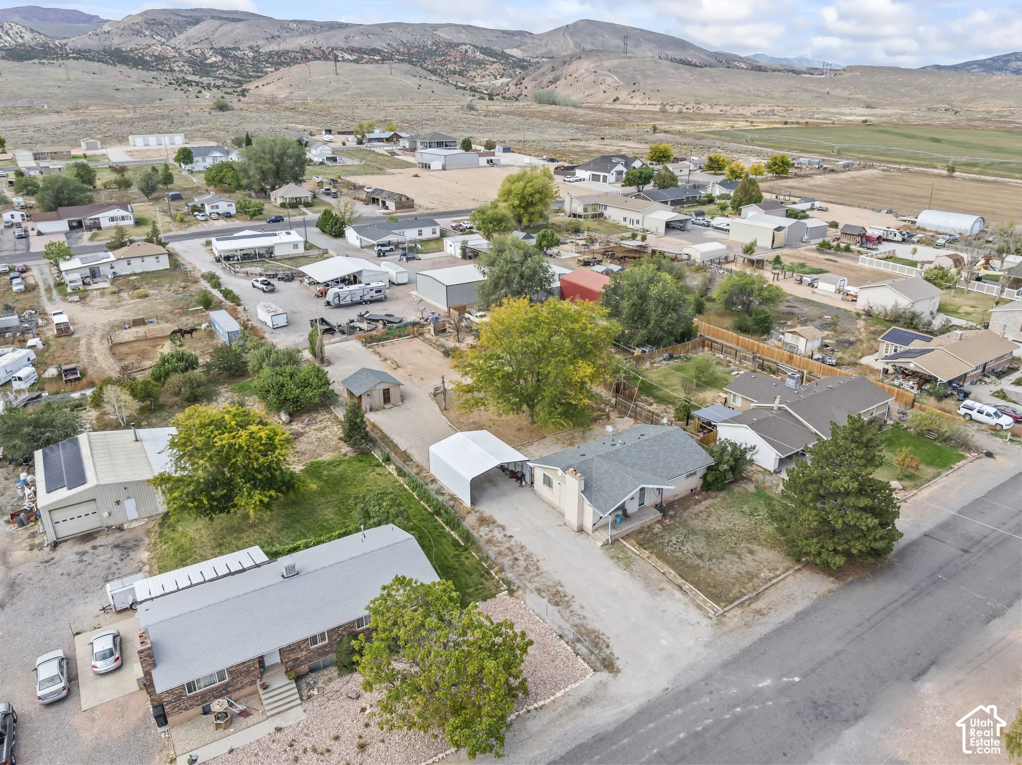 Aerial perspective of a property featuring a detached garage structure, a metal carport, mature trees, and a mountain range backdrop