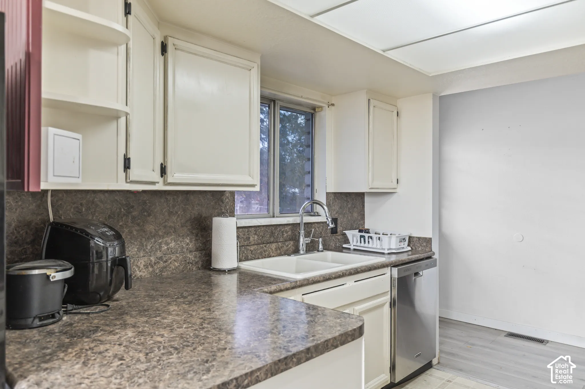 Kitchen featuring white cabinetry, solid-surface countertops with an integrated backsplash, double-basin sink with a gooseneck faucet, stainless steel dishwasher, and recessed ceiling lighting