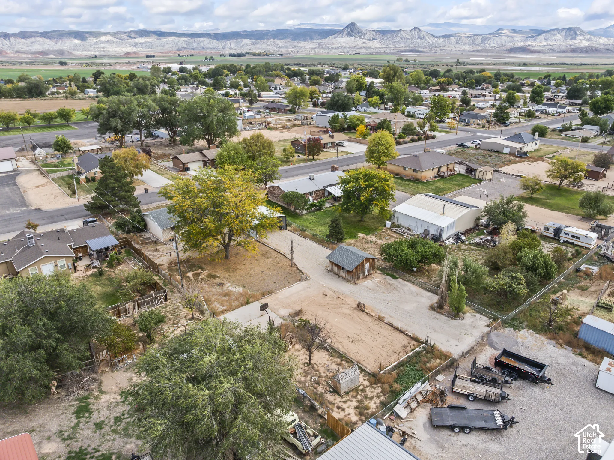 Aerial perspective featuring expansive open lot, mature trees, detached storage structure, and prominent mountain backdrop