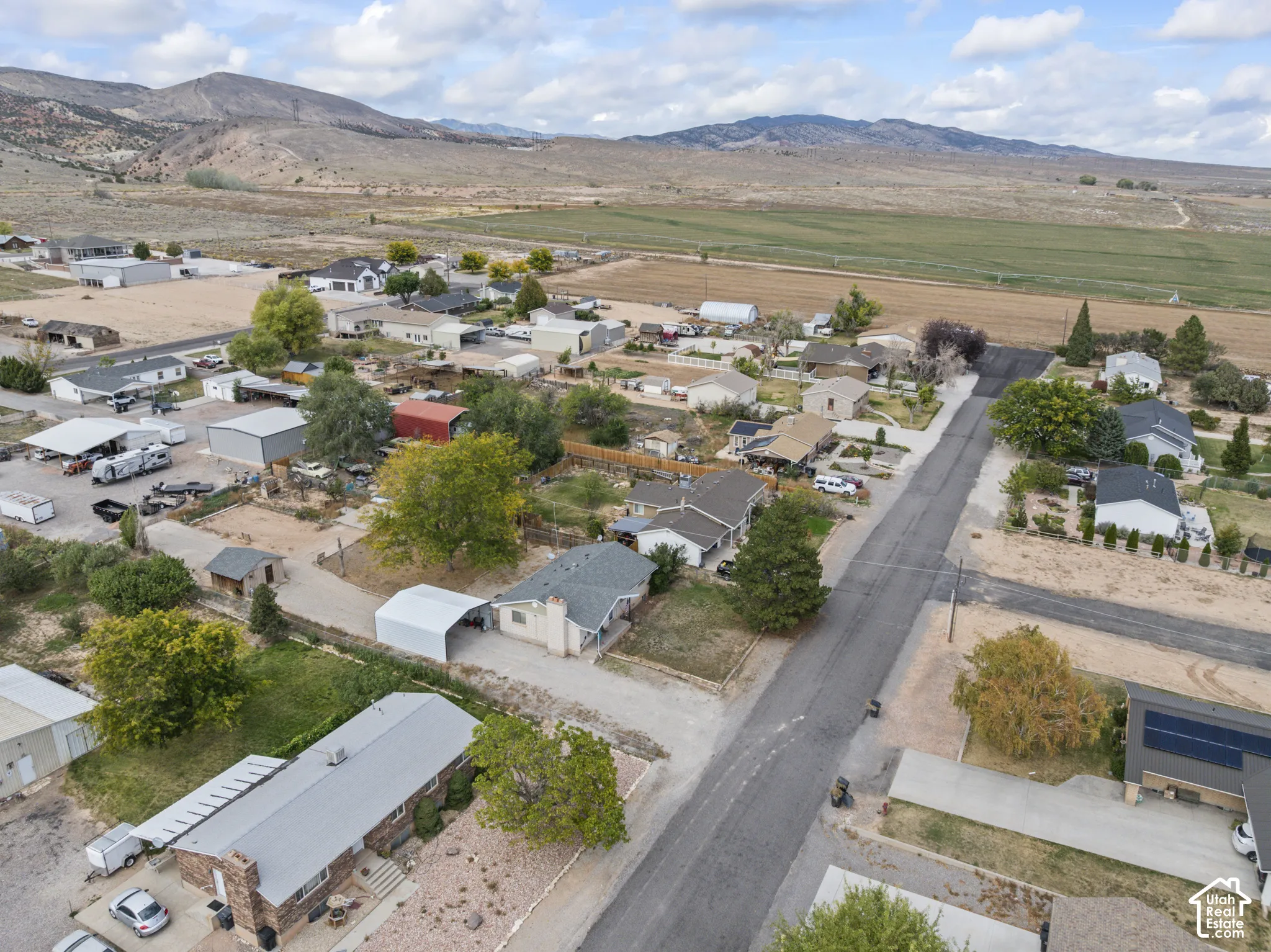 Aerial perspective featuring residential lots, mature trees, paved roadways, and a backdrop of mountains