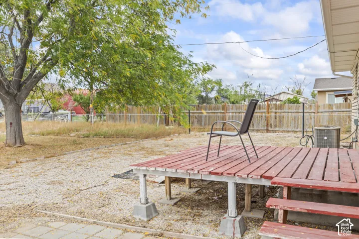 Backyard featuring a raised wooden deck, mature tree, stone-covered ground, and perimeter wood fencing