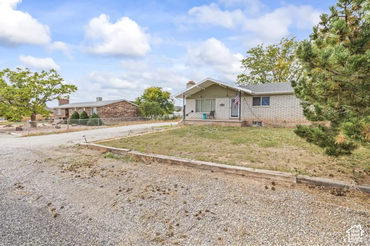 Single-story residence featuring a brick veneer exterior, covered front porch, timber retaining wall, and gravel driveway