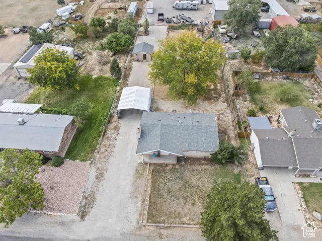 Aerial perspective of a property featuring a single-story residence, a metal carport, a detached shed, mature trees, and a fenced lot