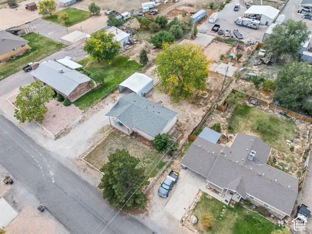 Aerial view featuring an expansive lot, mature trees, a detached metal carport, and a gravel driveway