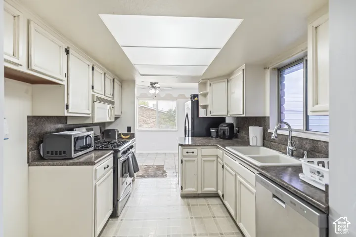 Kitchen featuring white cabinetry, dark-toned laminate countertops, a dual-basin sink with a gooseneck faucet, a built-in gas range, and recessed ceiling panel lighting
