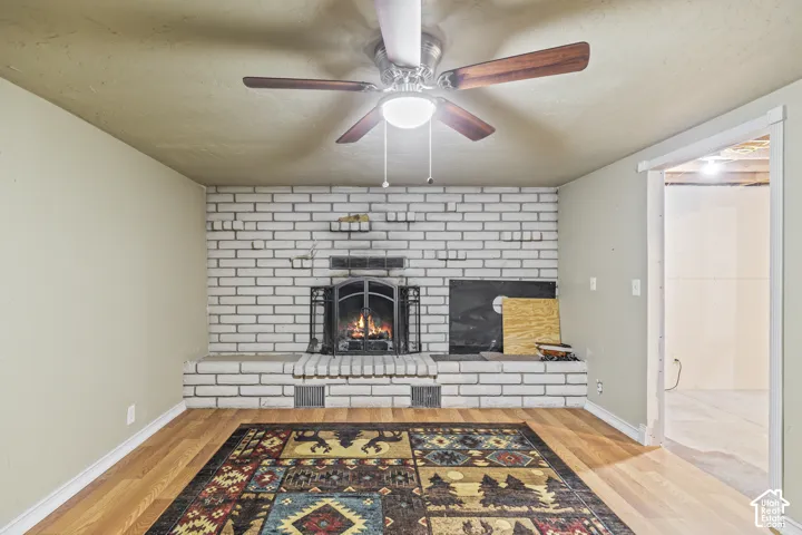 Painted brick fireplace with integrated hearth and decorative metal screen, complemented by a ceiling fan with integrated lighting and wood-finish flooring