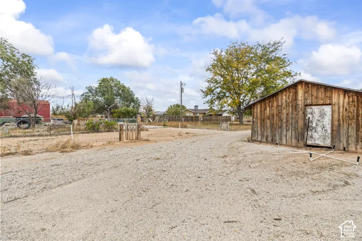 Expansive outdoor grounds featuring a gravel driveway, wood-sided outbuilding, wire perimeter fencing, and mature trees