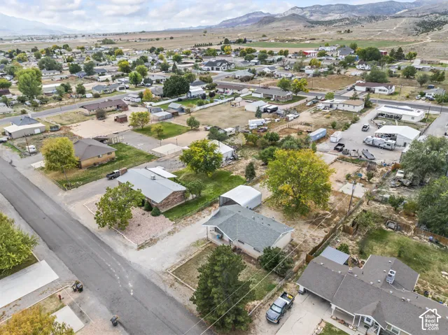 Aerial perspective featuring expansive residential lots, mature trees, mountain terrain, and paved street access