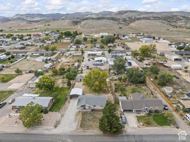 Aerial perspective of the residential lot featuring a detached carport, mature deciduous trees, gravel driveway, and a mountain range backdrop