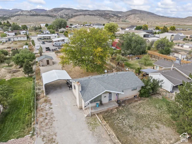 Single-story residence featuring light-colored masonry exterior, covered front porch, detached metal carport, storage shed, and mountain scenery