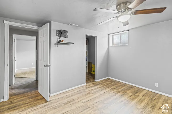 Room featuring wood-finish flooring, textured gray walls, a ceiling fan with integrated lighting, and a high-set window