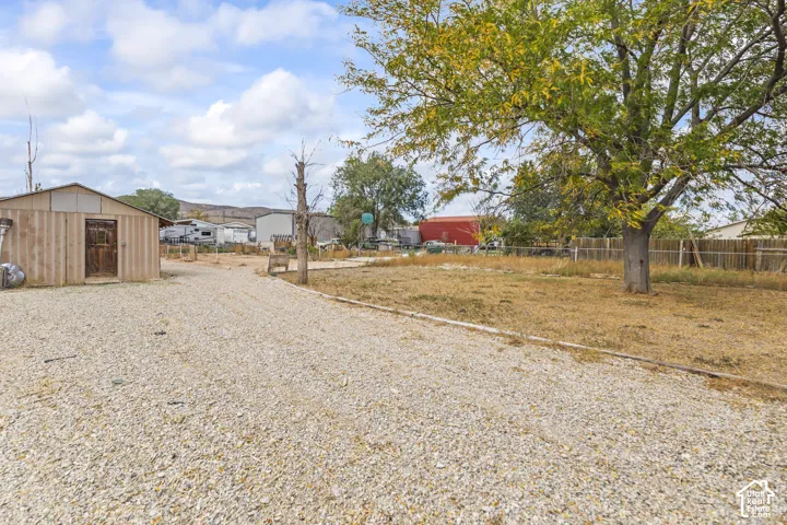 Expansive lot featuring a detached wood-frame structure, extensive gravel ground cover, and mature trees enclosed by wood fencing