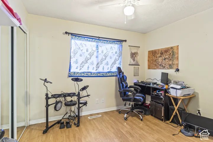 Room featuring wood-finish flooring, sliding mirror-paneled closet doors, and a ceiling-mounted light fixture with an integrated fan