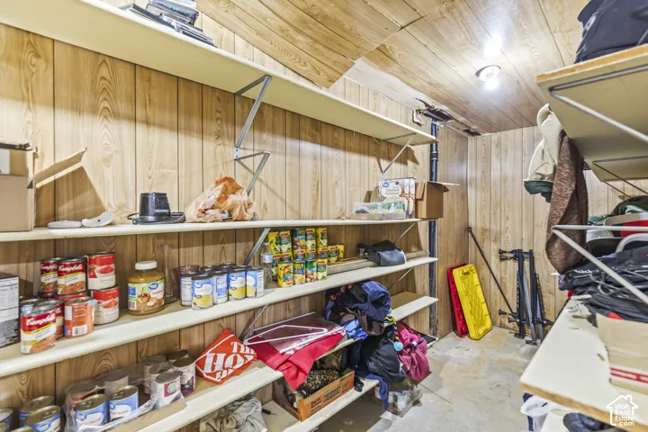 Storage space featuring wood-panel wall treatment, ceiling paneling, and multiple levels of built-in shelving with metal support brackets