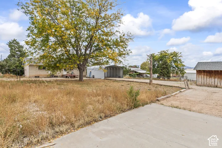 Exterior lot featuring a brick-sided residence, metal carport, wood-sided detached structure, and mature tree