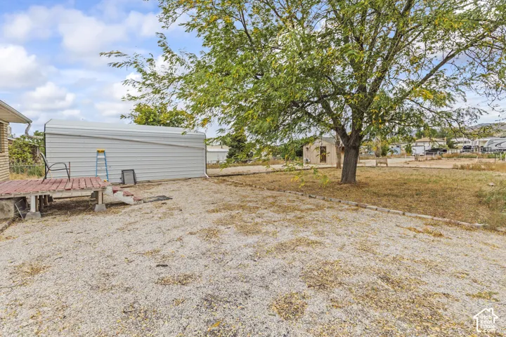 Expansive grounds featuring a mature shade tree, gravel surfacing, a raised wooden deck, and a detached metal structure