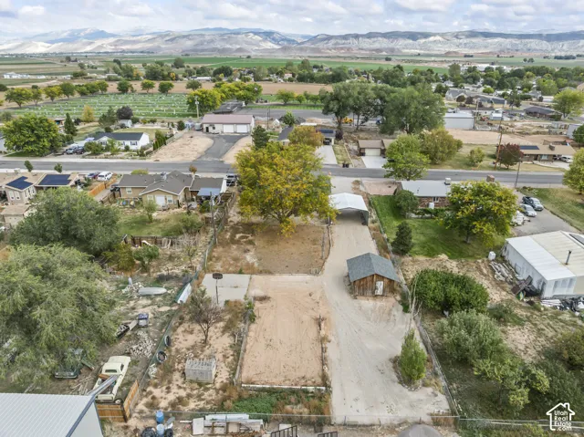 Expansive property featuring a gravel driveway, detached wood-sided storage structure, metal-roofed carport, mature trees, and mountain range backdrop