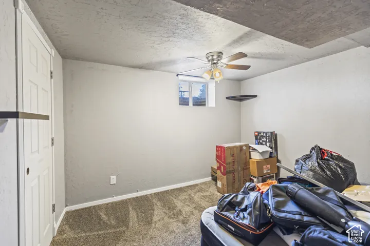 Neutral interior room featuring neutral-tone carpeting, textured wall finish, a ceiling fan with integrated lighting, and a built-in corner shelf