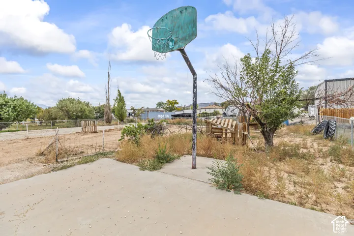 Concrete pad featuring a fixed basketball hoop, chain-link perimeter fencing, and mature trees