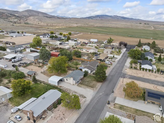 Aerial perspective featuring residential lots, mature trees, paved roadways, and a backdrop of mountains