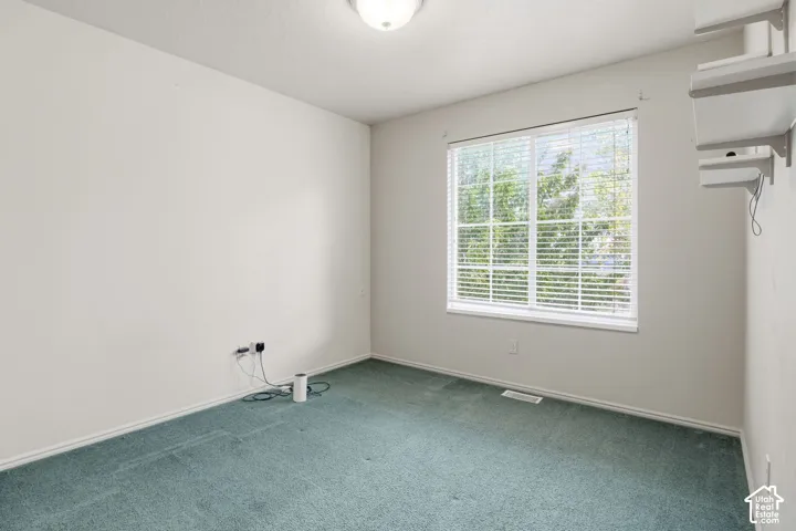 Interior space featuring neutral-toned wall paint, teal carpeting, a multi-pane window with installed blinds, and wall-mounted shelving