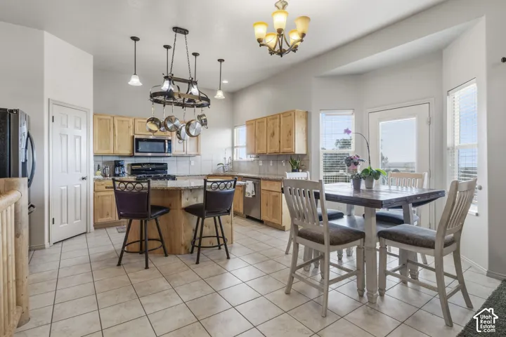Kitchen featuring light wood cabinetry, stone countertops, central kitchen island with overhead pot rack, tile flooring, and a multi-light chandelier