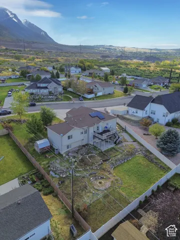Aerial perspective showcasing a multi-level residence with roof-mounted solar panels, an elevated rear deck, a fenced perimeter, and a mountainous backdrop