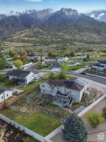 Two-story residence featuring an elevated deck, ground-level patio, solar panel array, fenced yard, and mountain backdrop