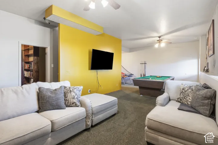 Open-concept room featuring wall-to-wall carpeting, dual ceiling fans, a custom structural accent wall with recessed lighting, and a built-in shelving unit